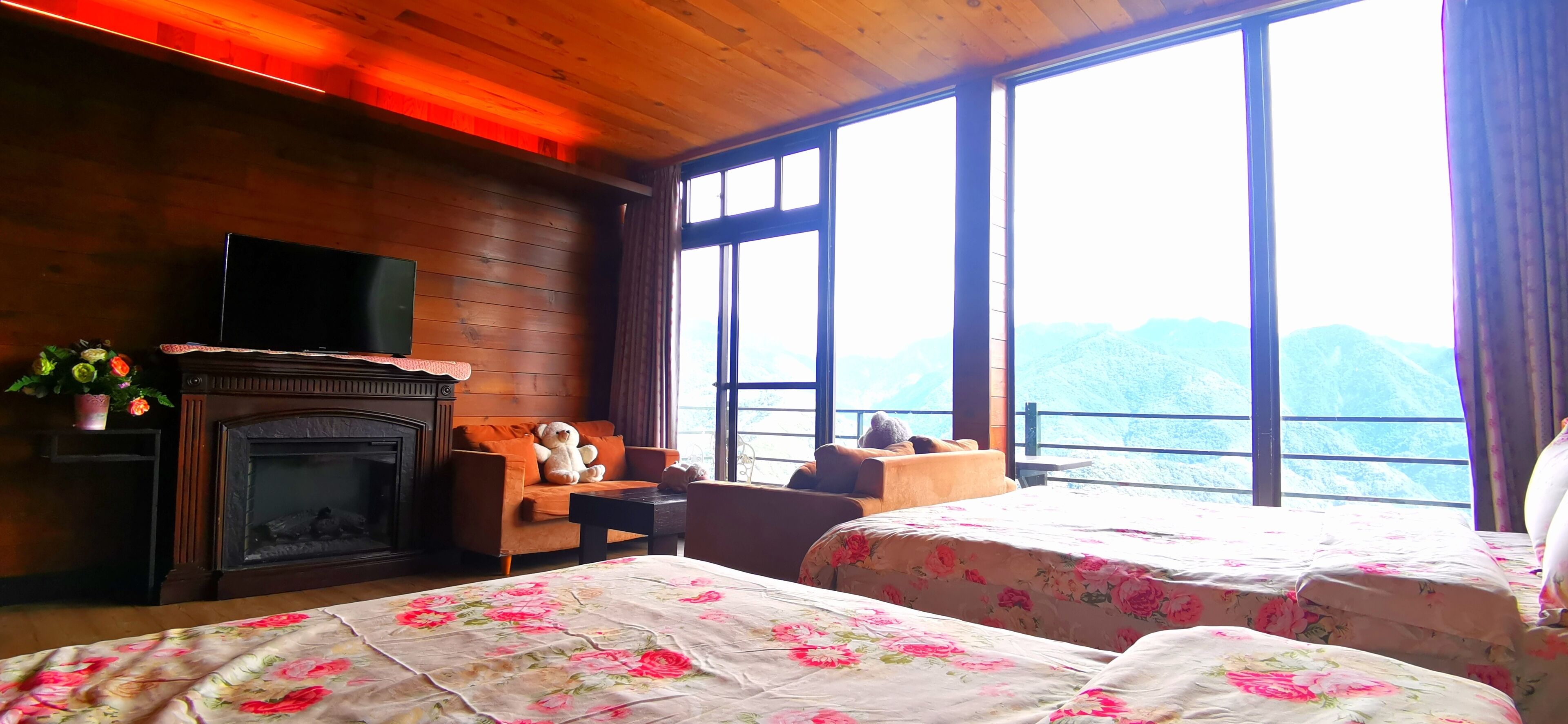A cozy room with a fireplace, a sofa, a TV, and two beds with floral bedding.