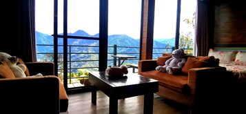 Una habitación acogedora con amplias ventanas que ofrecen vista a la montaña, una mesa de madera y dos sofás con cojines mullidos.