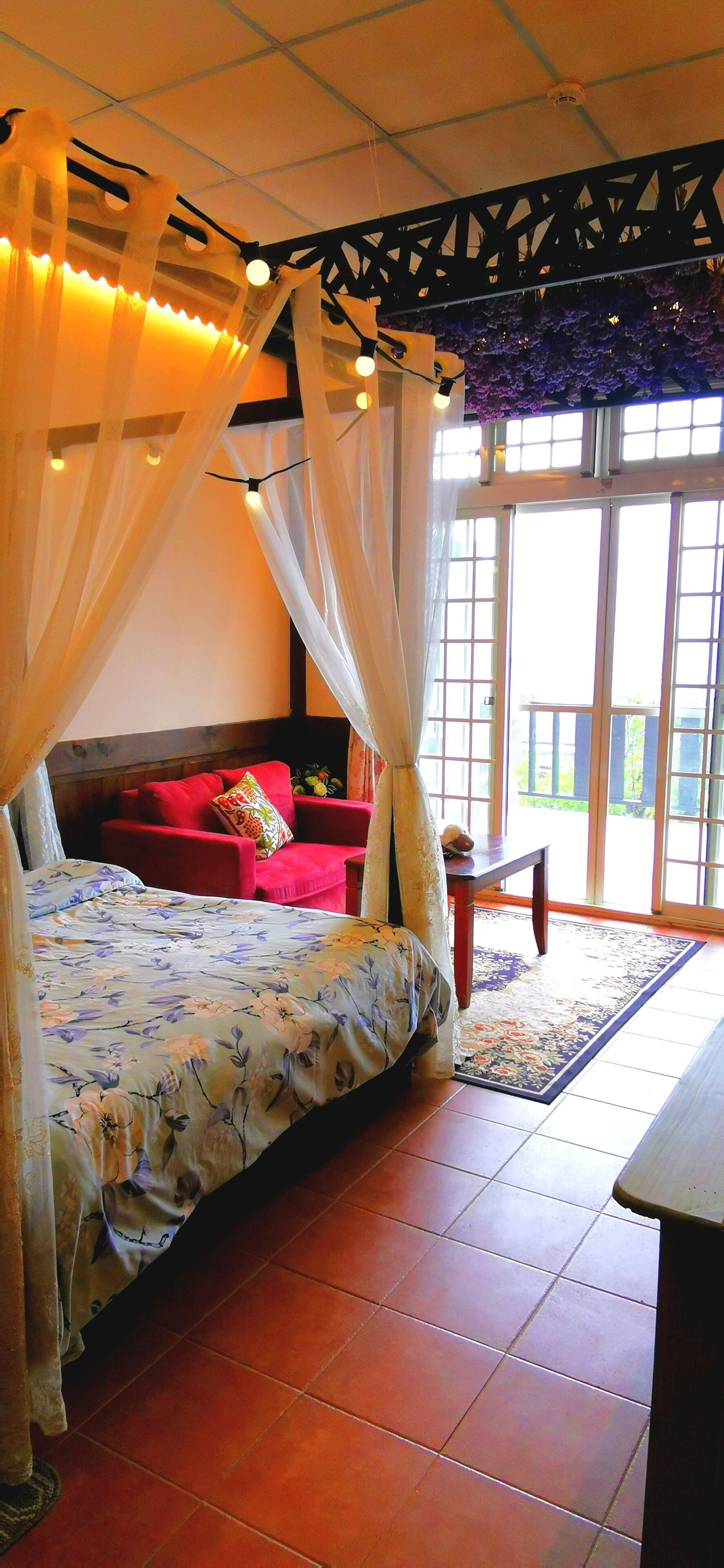 Ein Zimmer mit einem Bett, einem roten Sessel und Blick durch große Fenster.