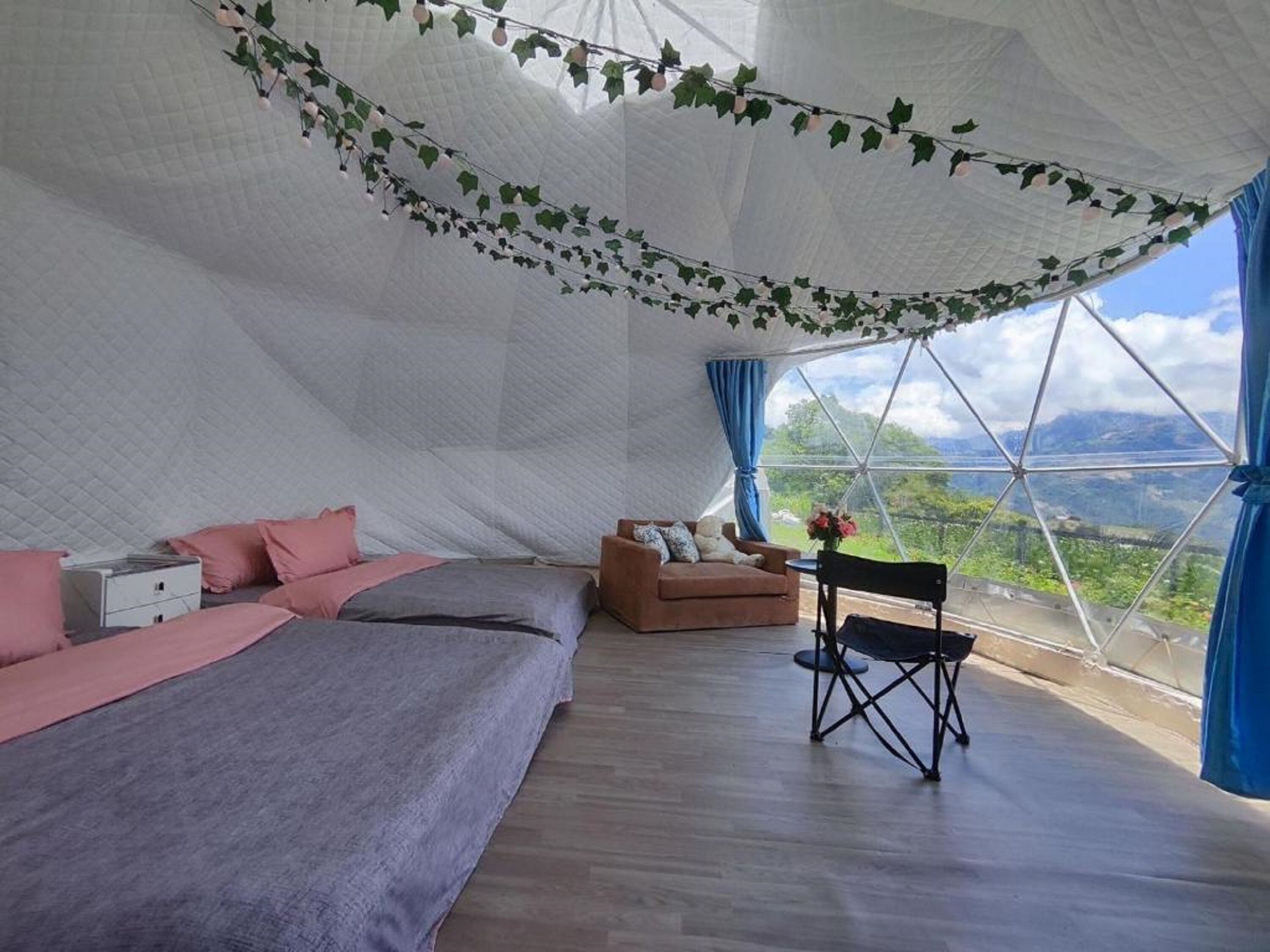Une chambre confortable avec un lit, un canapé et un fauteuil, le tout disposé sous une grande structure ressemblant à une tente, offrant une vue sur l’extérieur.