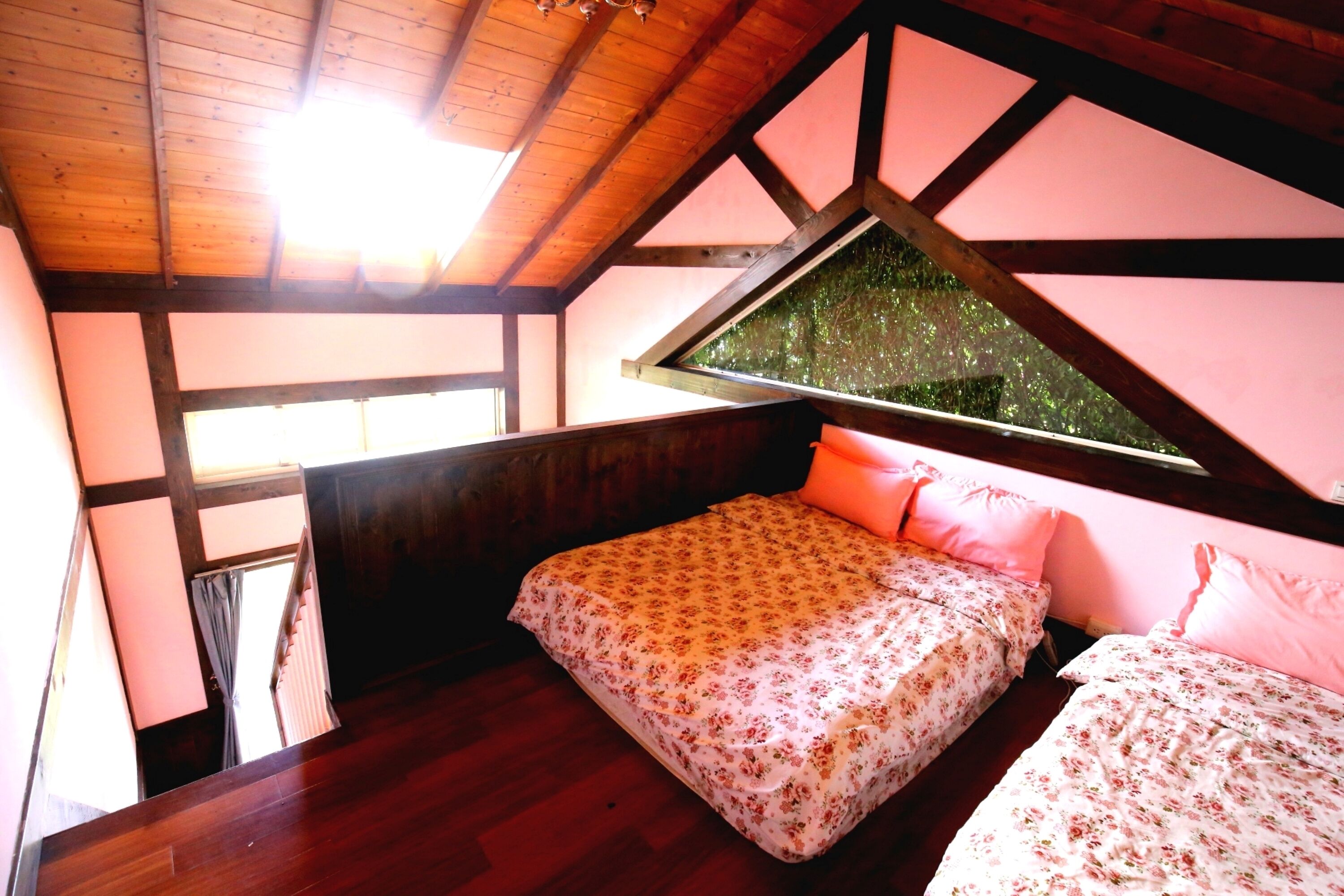 A bedroom with a wooden ceiling, a large window with a view of trees, a bed with floral bedding, and a wooden floor.