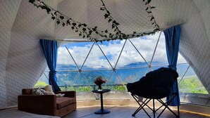Una habitació acollidora amb vista a un paisatge muntanyós, un sofà confortable, una taula petita amb un ram i una cadira.