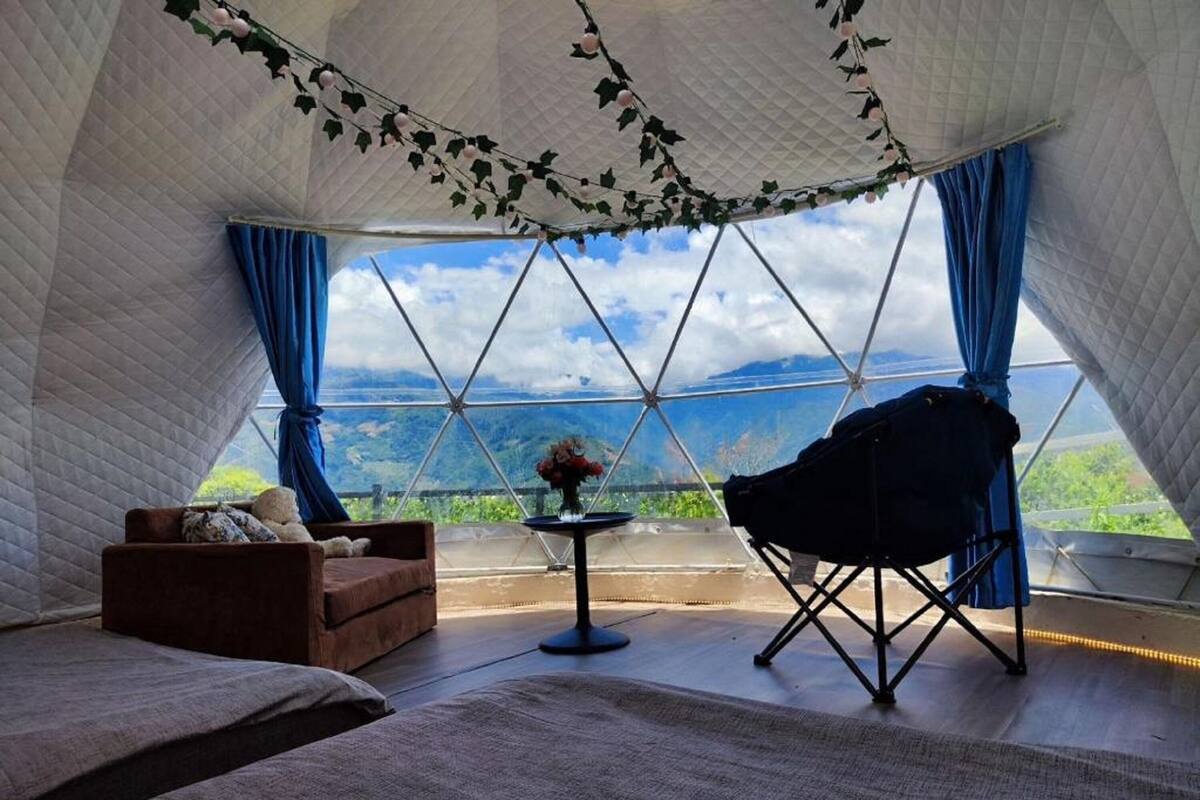A cozy room with a view of a mountainous landscape, a comfortable sofa, a small table with a vase, and a chair.