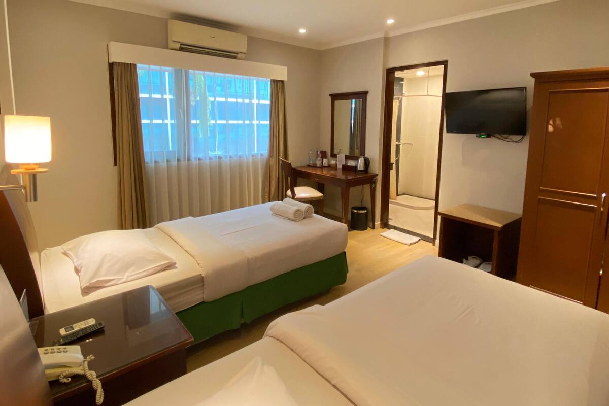 Habitación de hotel con dos camas, un escritorio con teléfono, un espejo, un televisor y un equipo de aire acondicionado.