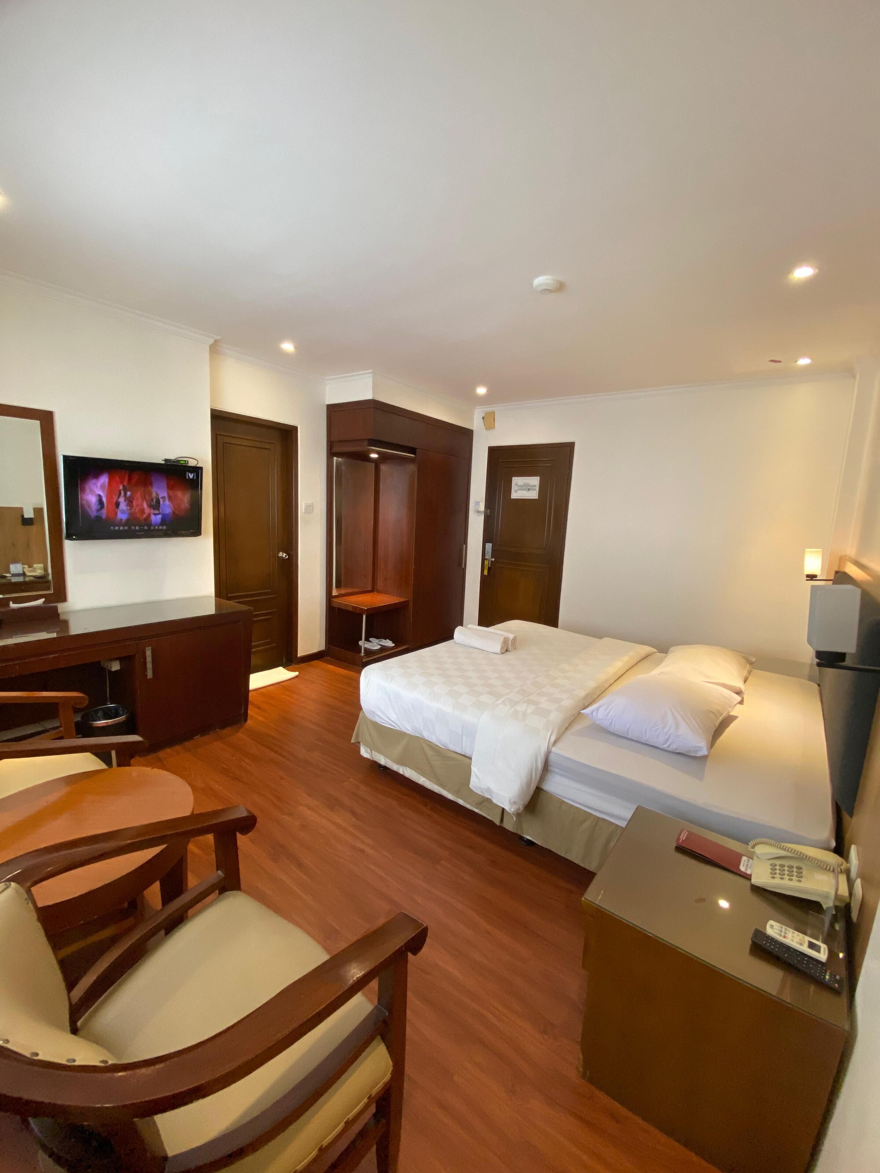 A hotel room with a bed, a desk, a chair, a television, and a wardrobe.