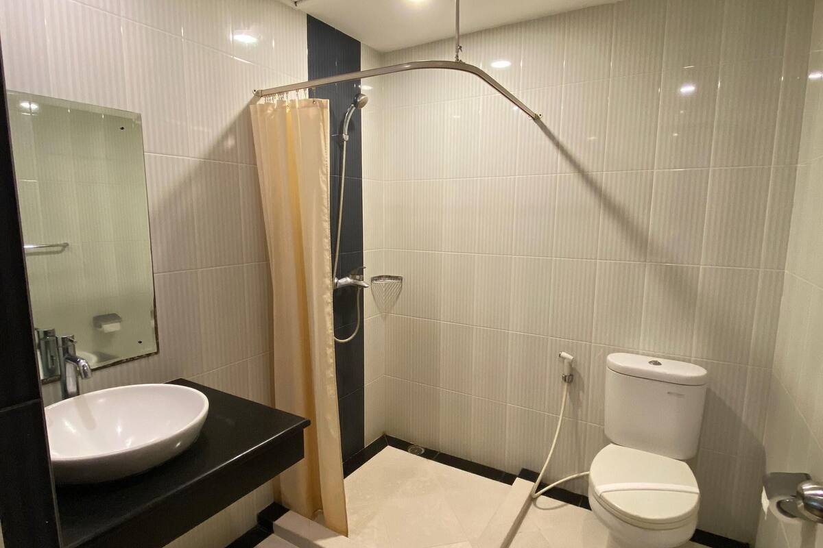 Un baño con un lavabo blanco, encimera negra, ducha con cortina beige, inodoro y espejo.