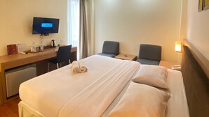 Una habitación de hotel con una cama grande, un escritorio con televisor, dos sillas y una mesita pequeña.