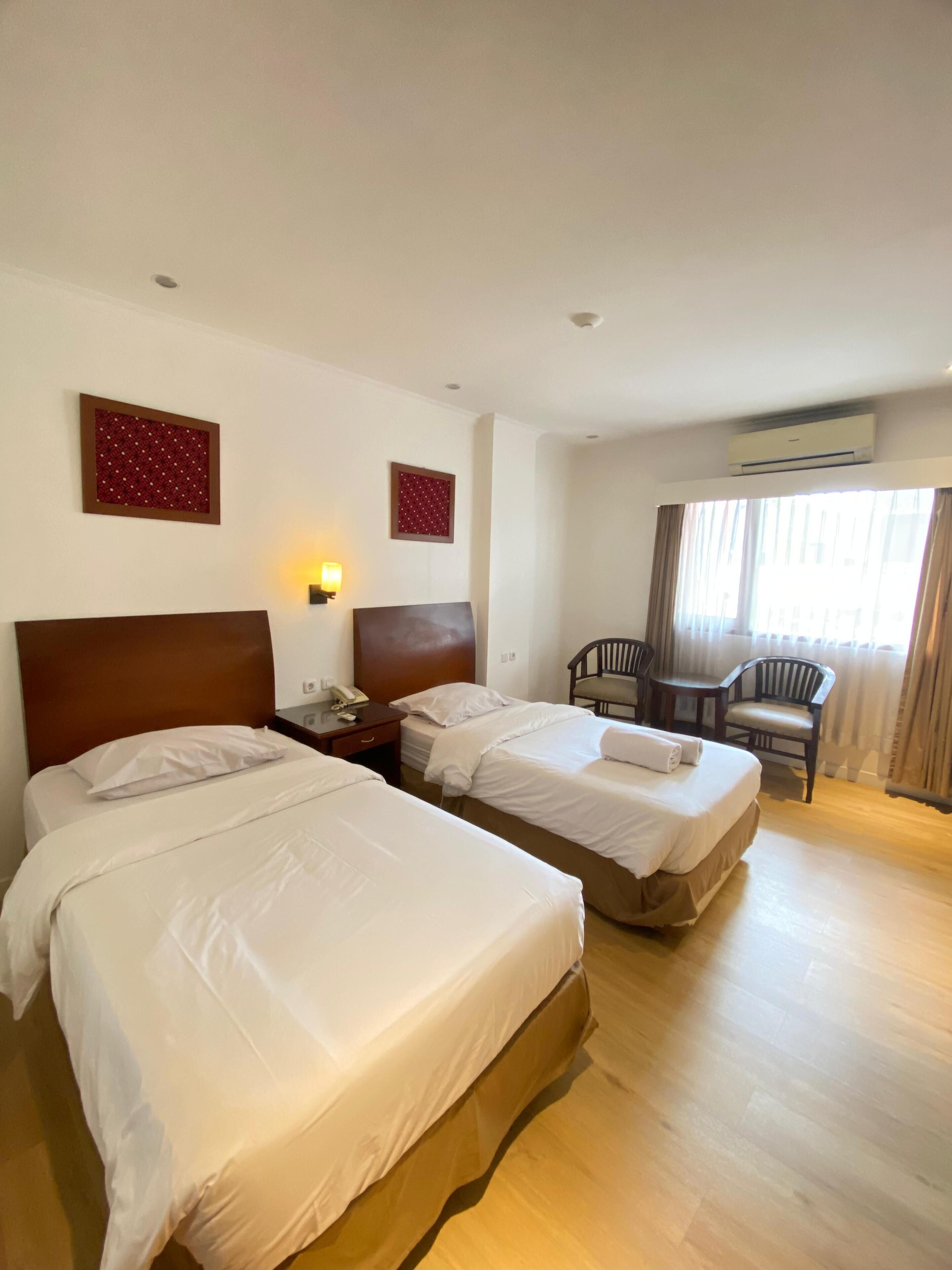 A hotel room with two beds, a desk, a chair, and an air conditioning unit.