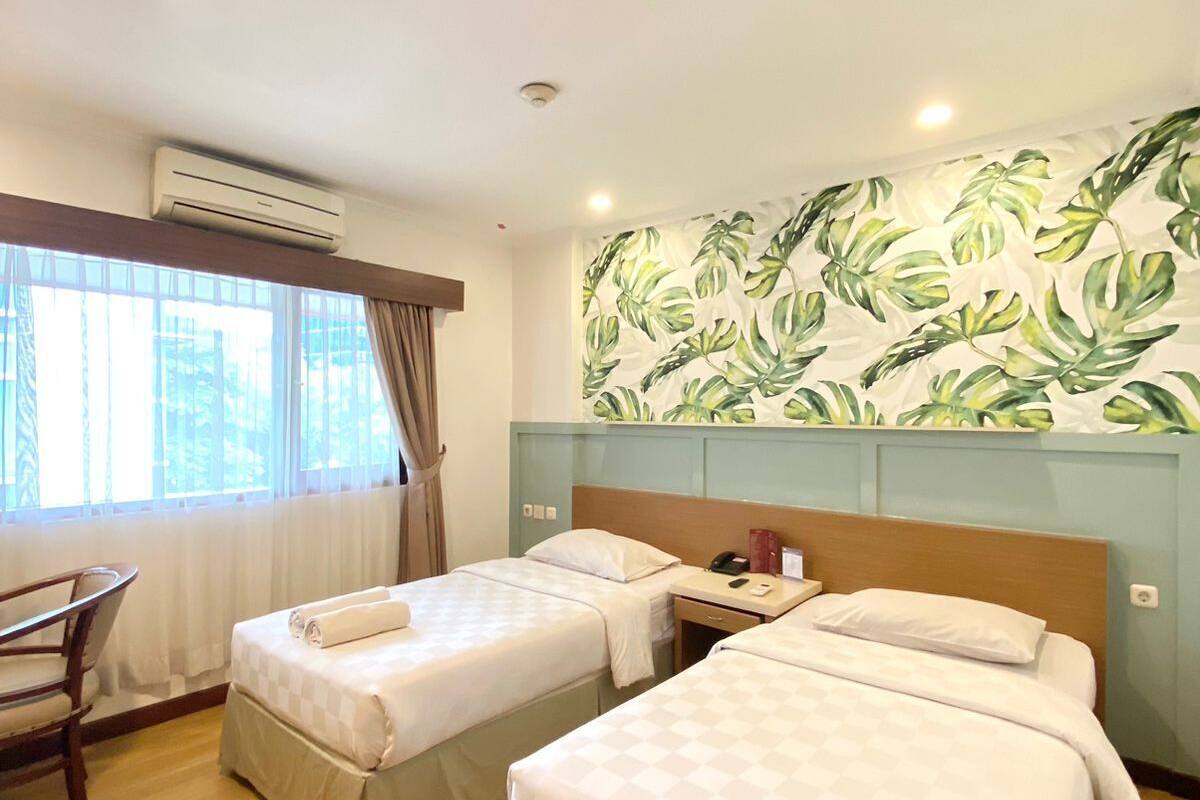 Habitación de hotel con dos camas, un escritorio y una ventana con cortinas.