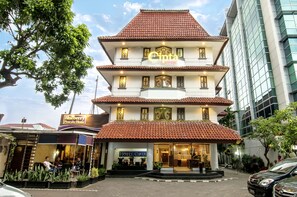 Een hotel met meerdere verdiepingen, voorzien van een traditioneel betegeld dak, met een zichtbaar bord voor 'Hotel Cipta' en een 'Blueberry Pancake House' ernaast.