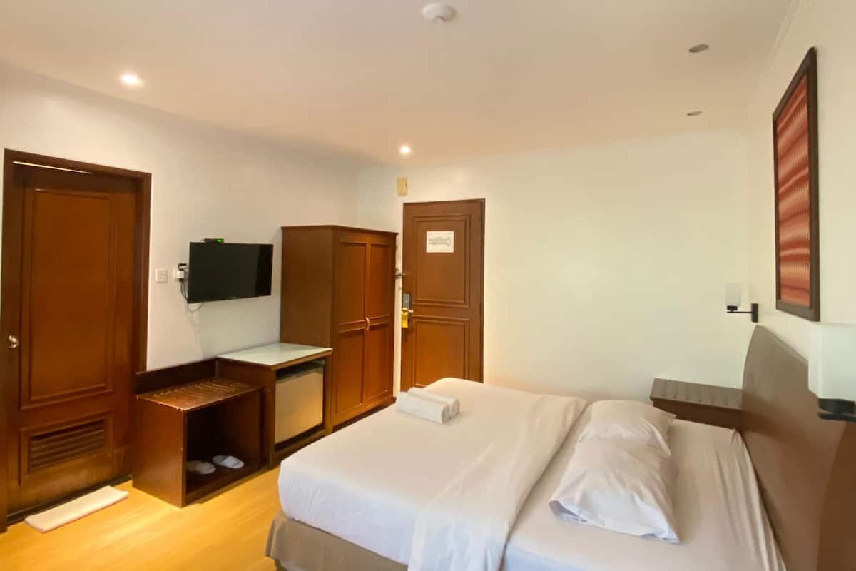 Una habitación de hotel con una cama, un armario de madera, un escritorio con teléfono y un televisor en la pared.