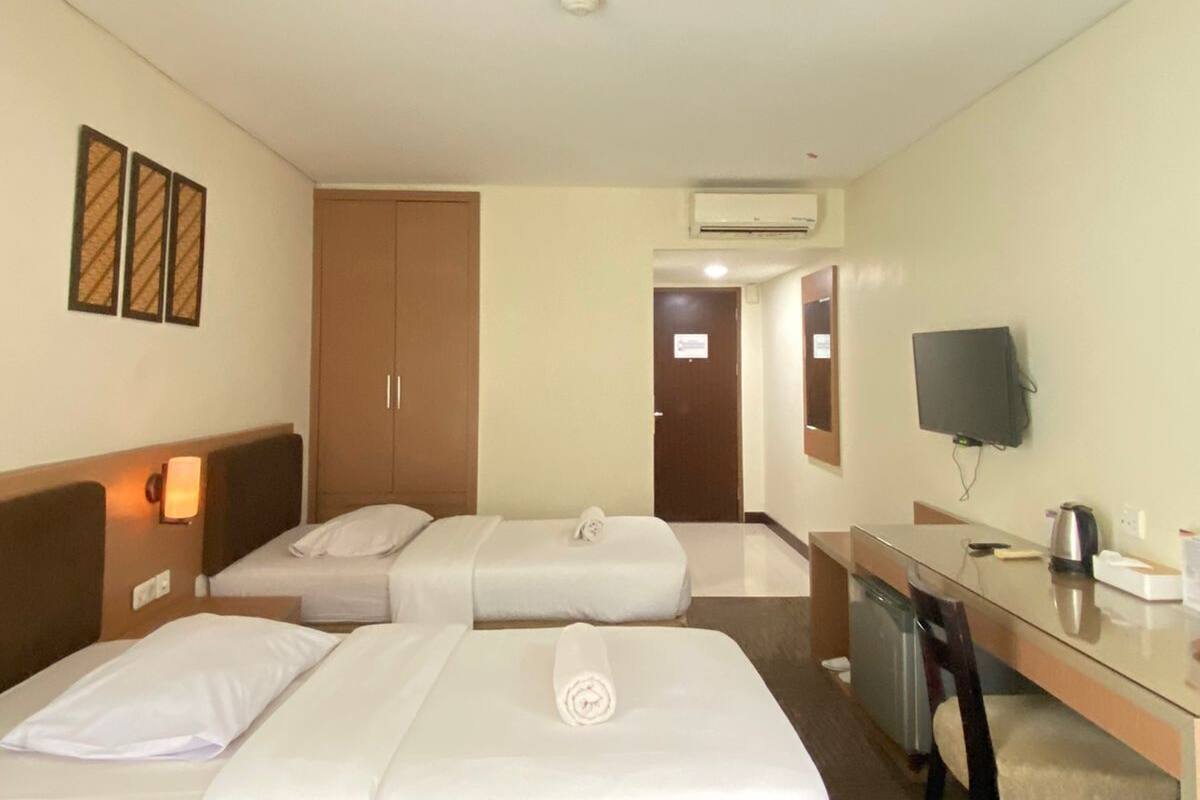 Habitación de hotel con dos camas, un escritorio, una silla, un televisor y un equipo de aire acondicionado.