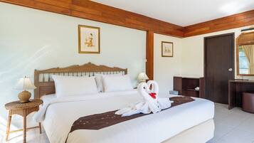 A hotel room with a large bed, wooden headboard, two framed pictures on the wall, a desk with a lamp, and a door with a view.