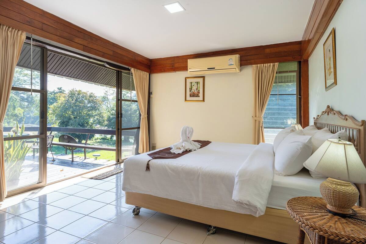 A hotel room with a large bed, a balcony, and a view of greenery.