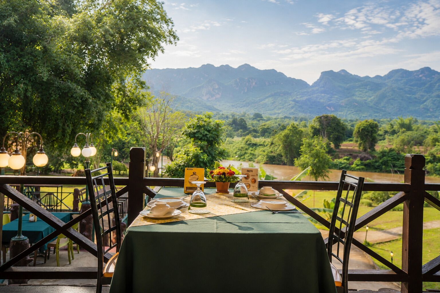 An outdoor dining area with a table set for two, overlooking a mountainous landscape.