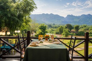 Un espace de restauration en plein air avec une table dressée pour deux personnes, offrant une vue sur un paysage montagneux.