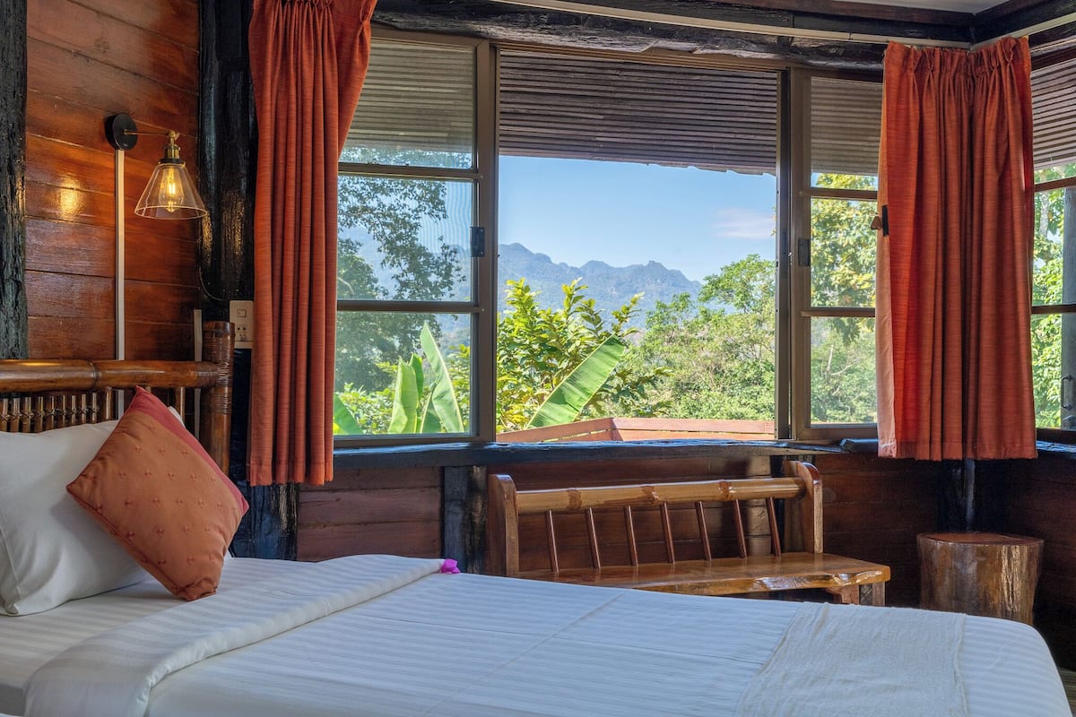 A wooden room with a bed, a bench, and a window with curtains.