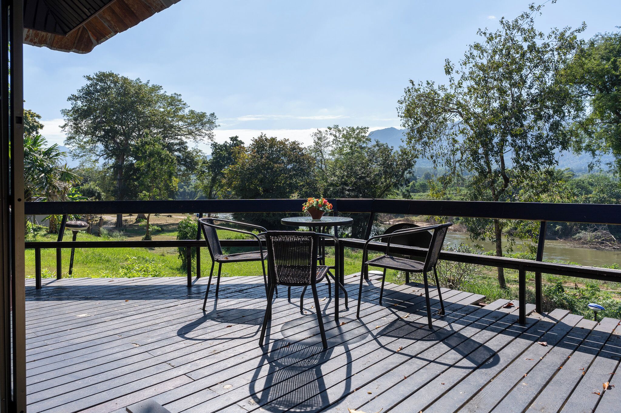 A wooden deck with a table and chairs, overlooking a river and trees.