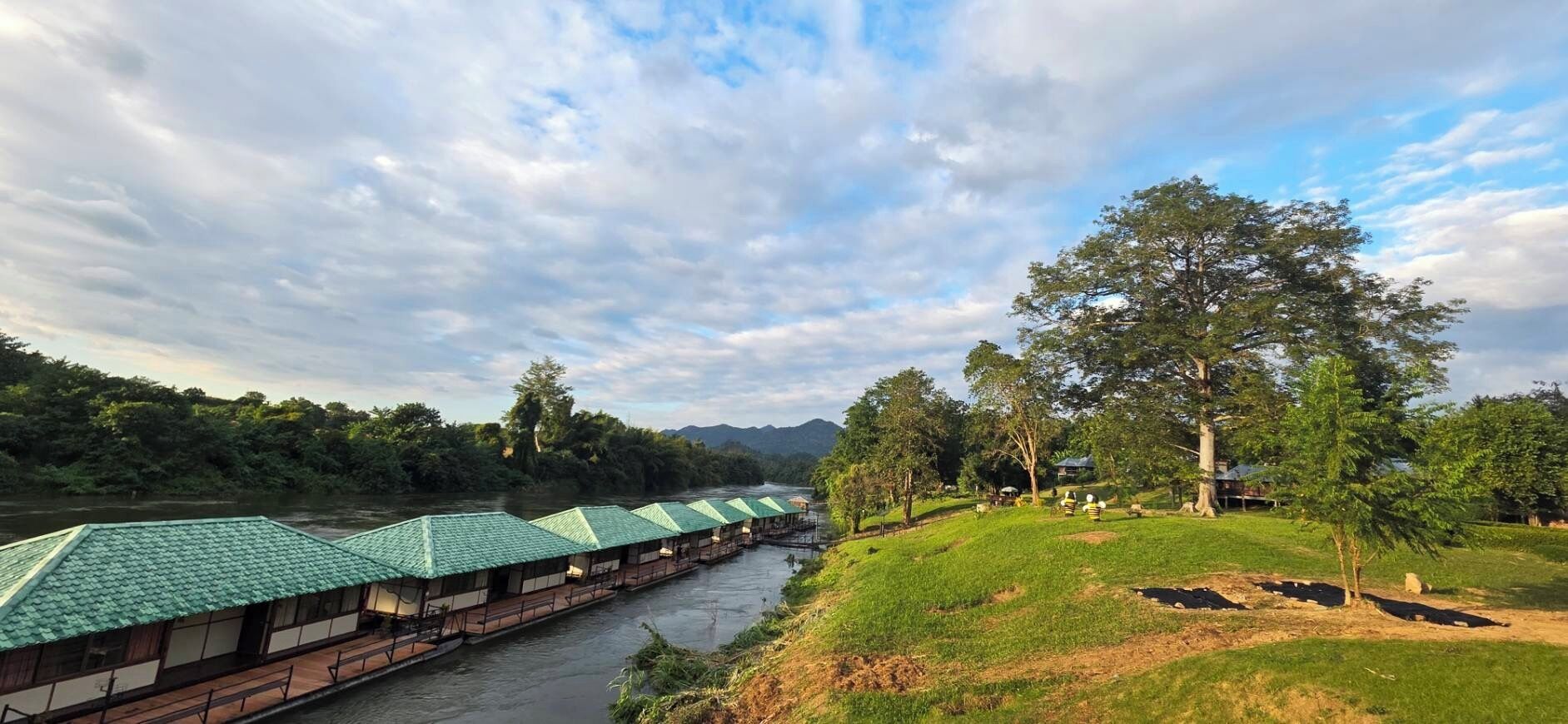 A riverside hotel with green-roofed buildings, a grassy area with trees, and a river.