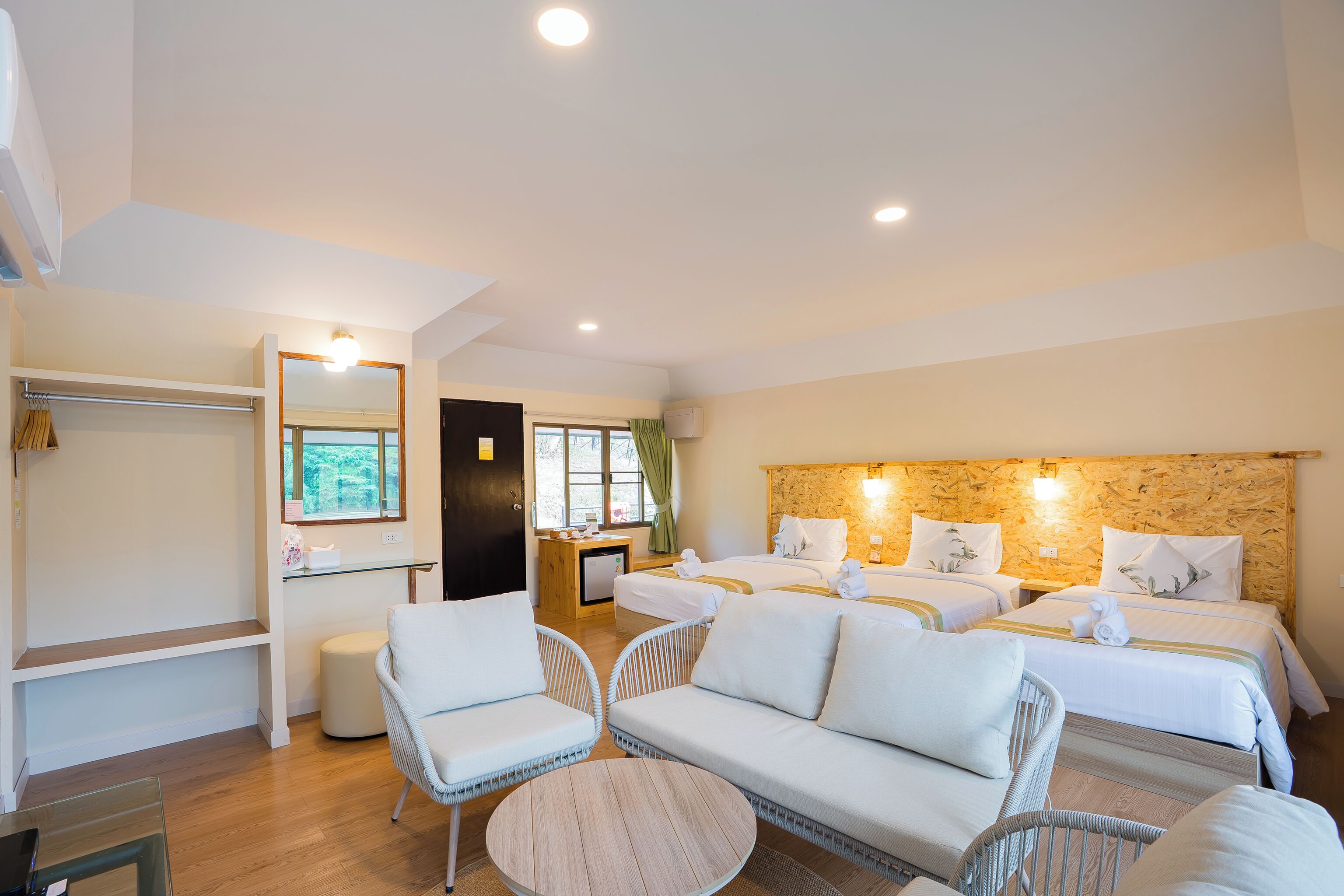 Une chambre d’hôtel avec un grand lit, deux petits lits, un canapé, une table basse ronde, un miroir, un petit bureau et une armoire.