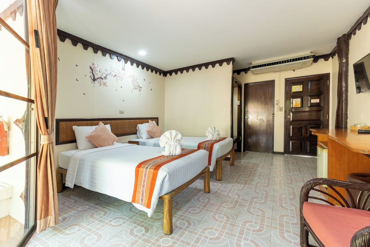 A hotel room with two beds, a wooden desk, a chair, and a TV on the wall.