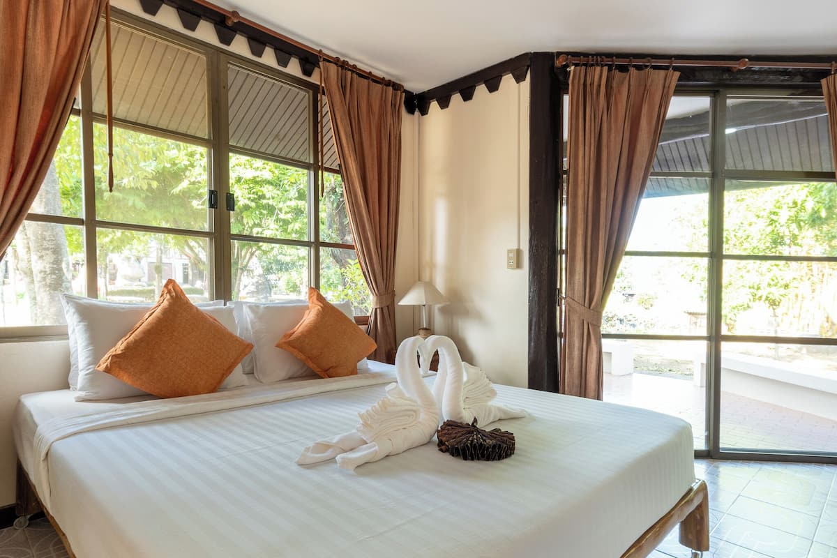 A hotel room with a large bed, two pillows, a lamp, and a window with curtains.