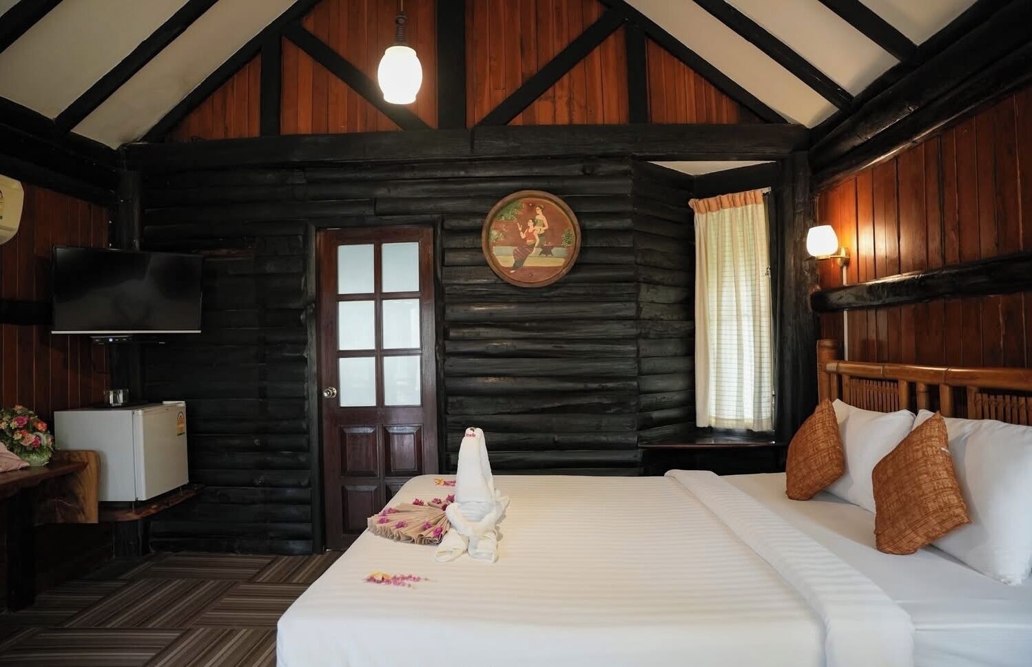 A log cabin-style room with a bed, a television, a door, and a window with curtains.