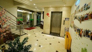 Vestíbulo de hotel con suelo de baldosas, un ascensor, una escalera y una pared decorada con fotografías.