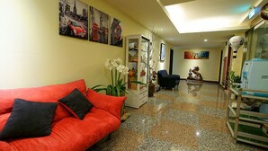 Un vestíbulo de hotel con un sofá rojo, un aparador de vidrio y una estatua de dos personas.