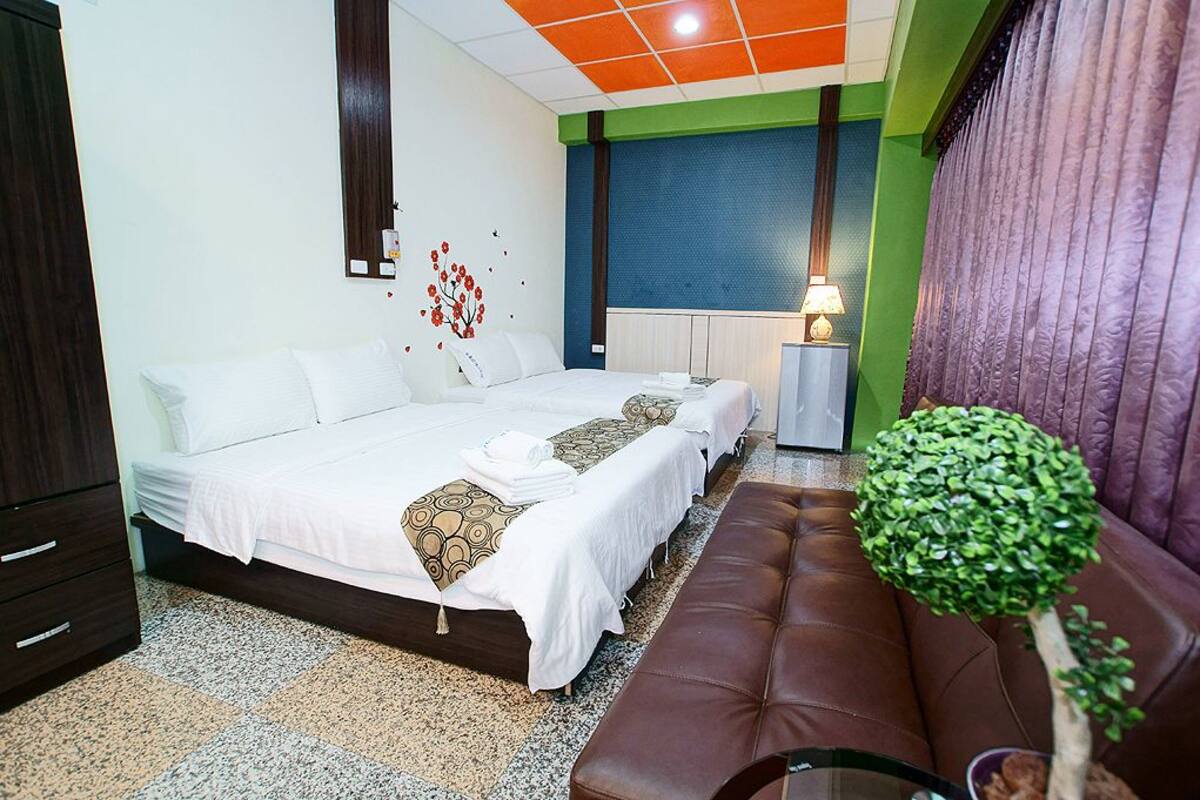 A hotel room with a bed, a bench, a small table, a lamp, and a plant.