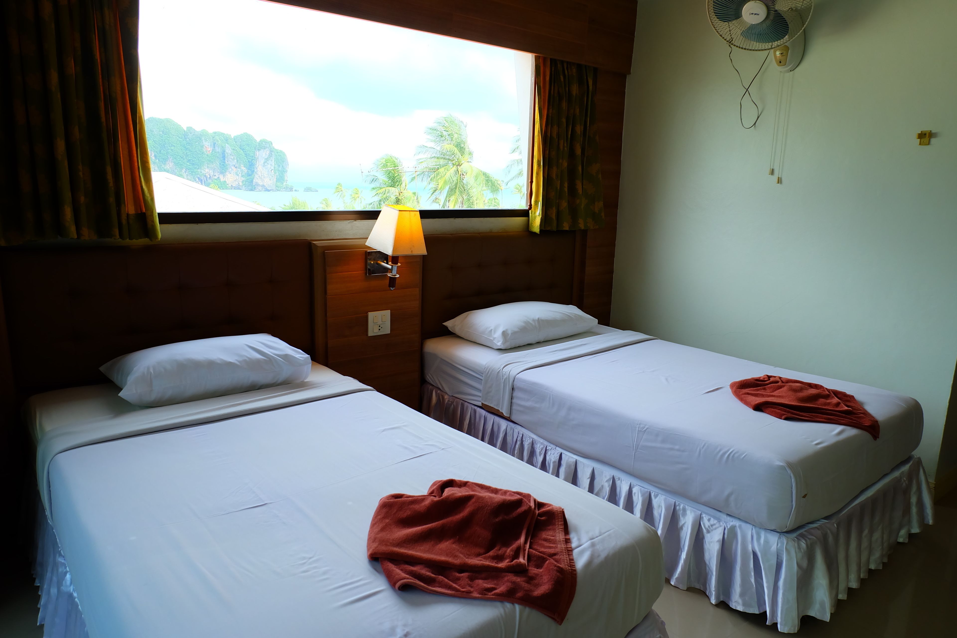 Une chambre avec deux lits, une table de chevet, une lampe et une fenêtre avec des rideaux.