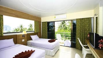 Quarto de hotel com duas camas, uma escrivaninha, televisão e varanda com vista para palmeiras.