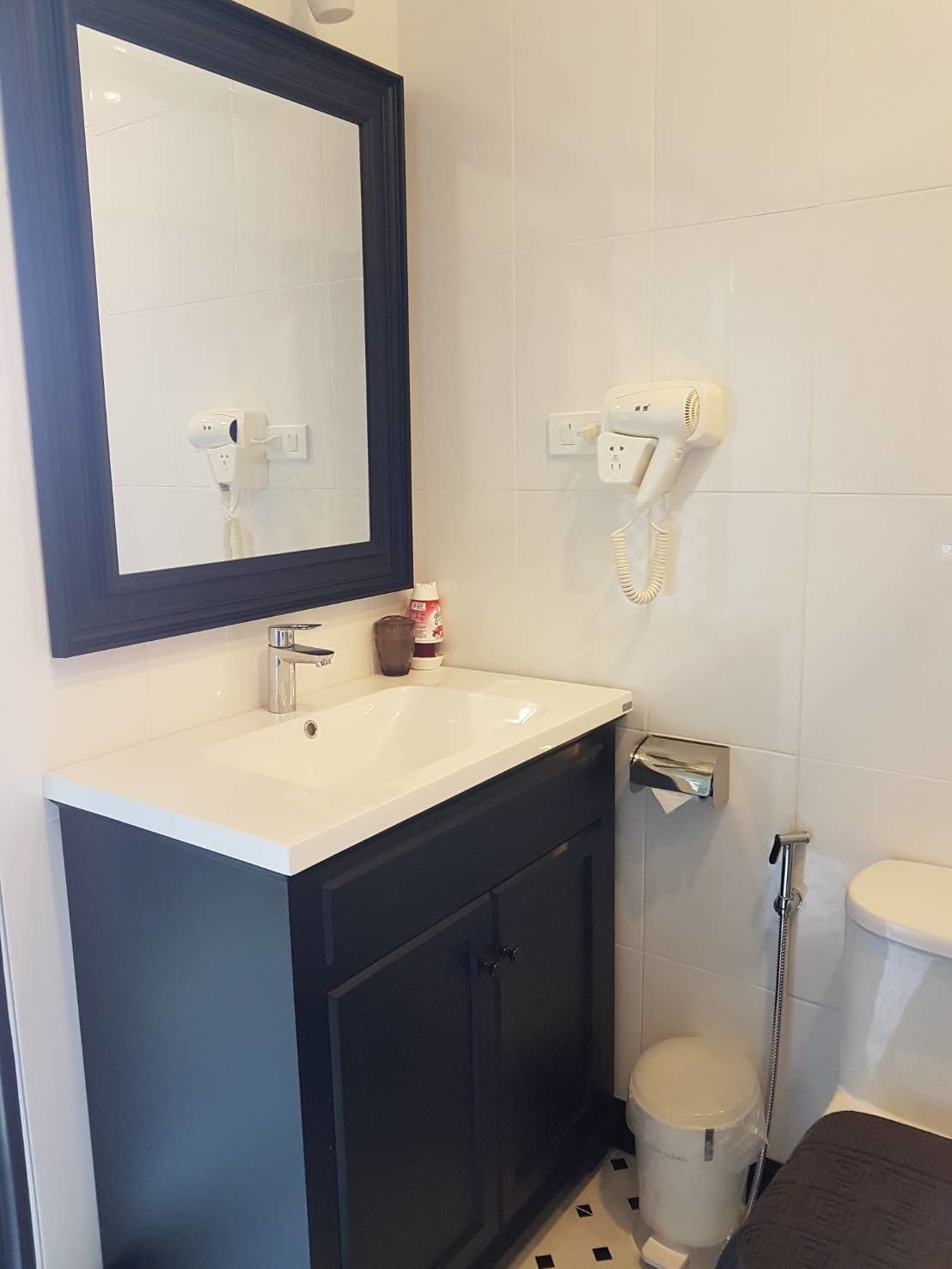 A bathroom with a white sink, dark cabinets, a mirror, a hairdryer, and a toilet.