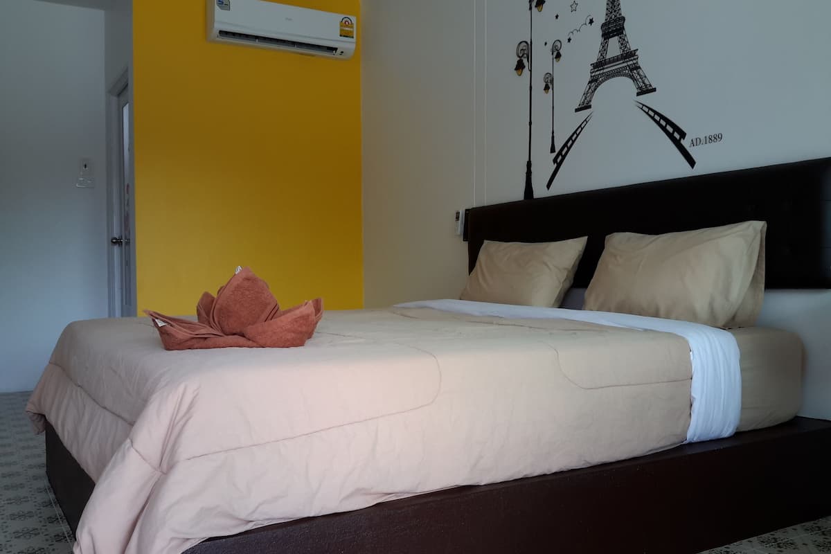 A bed with a beige bedspread and pillows, a brown towel, and a wall-mounted air conditioner.