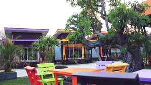 An outdoor seating area with colorful chairs and tables, surrounded by greenery and modern buildings. - D-Sine Resort (Buriram)