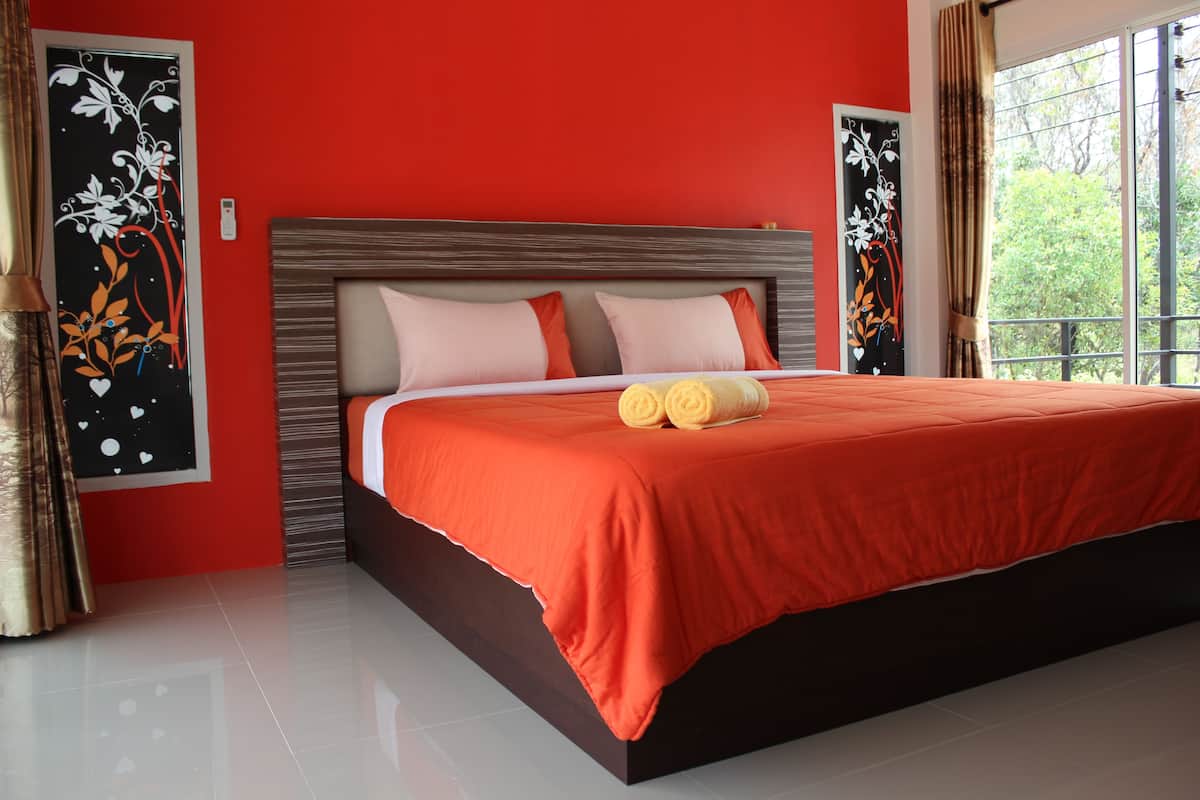 A modern bedroom with a large bed, red walls, and artwork on the walls.