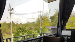 A balcony with a table and two chairs, a lamp, and a view of greenery and power lines. - D-Sine Resort (Buriram)