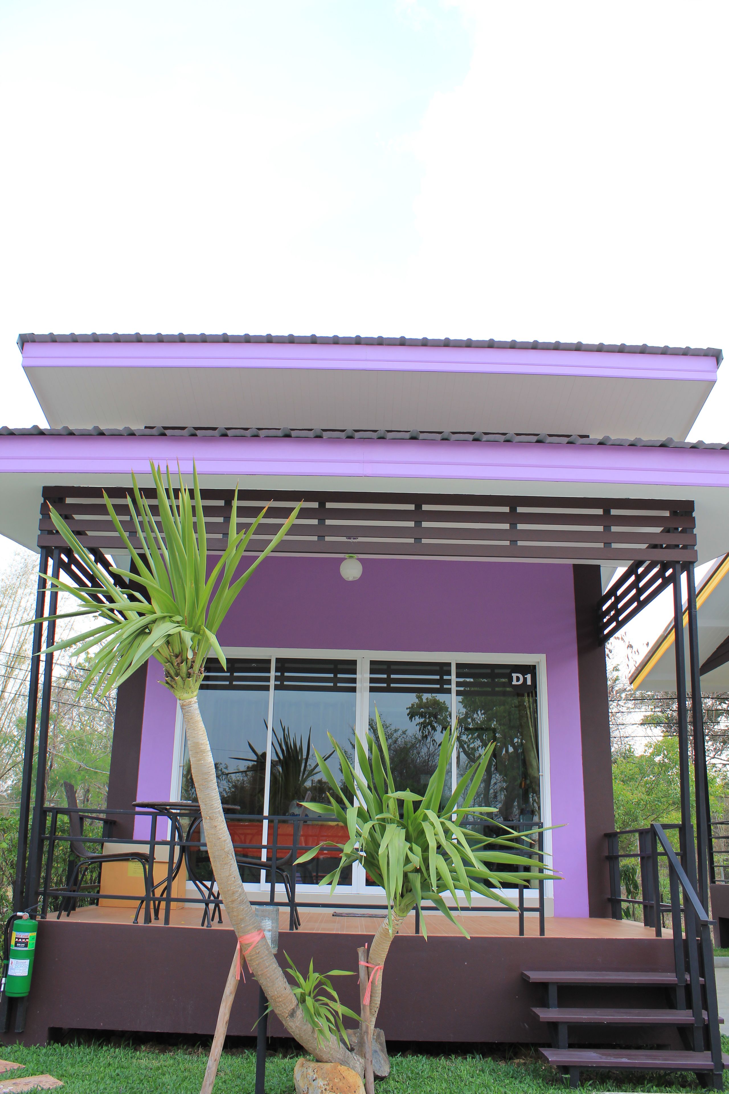 Un edificio moderno con fachada púrpura, grandes ventanales y un área de estar al aire libre cubierta con sillas y una mesa.
