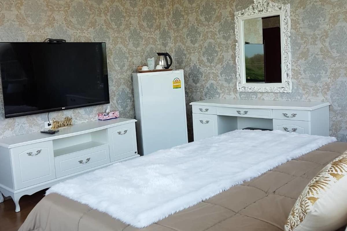 A bedroom with a large bed, a television, a refrigerator, a mirror, and a chandelier.