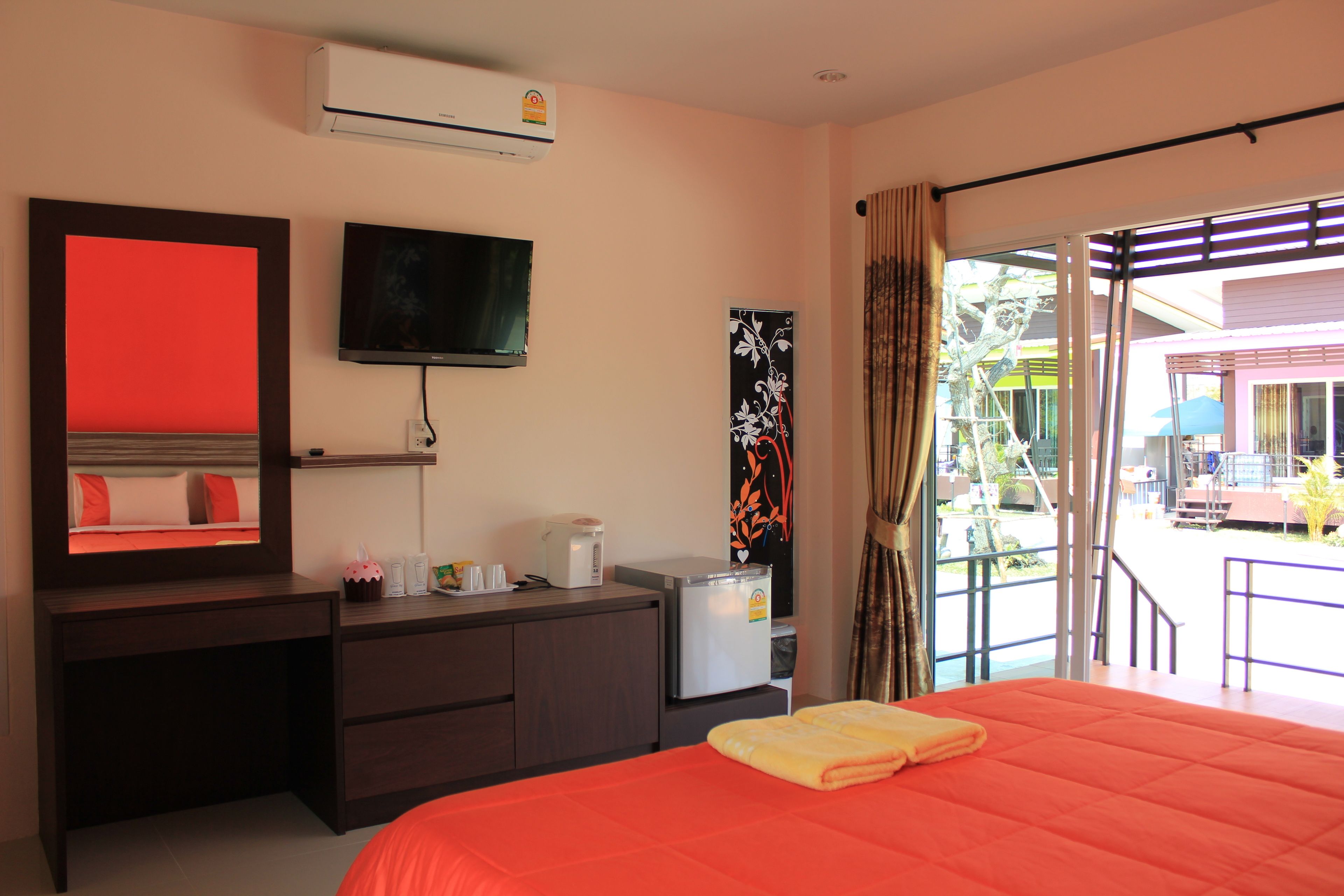 Quarto de hotel com cama, televisão, secretária com computador, frigorífico e janela com vista para o exterior.