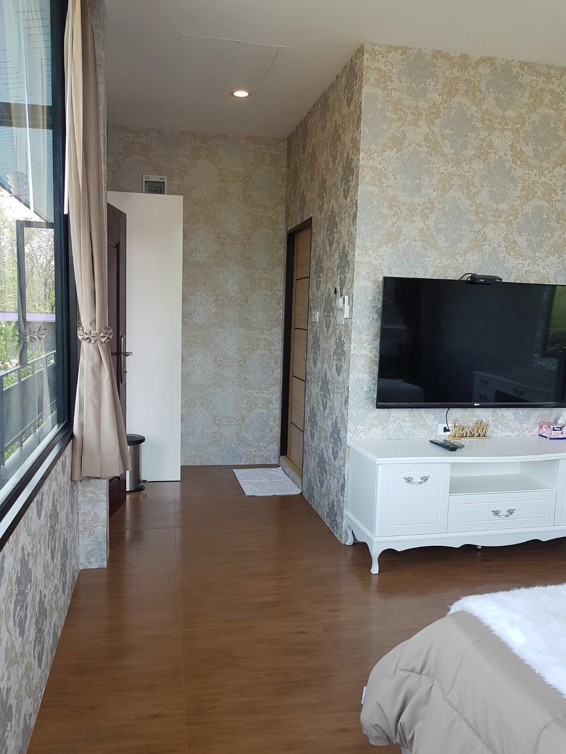 A bedroom with a large TV, a white dresser, and a window with curtains.