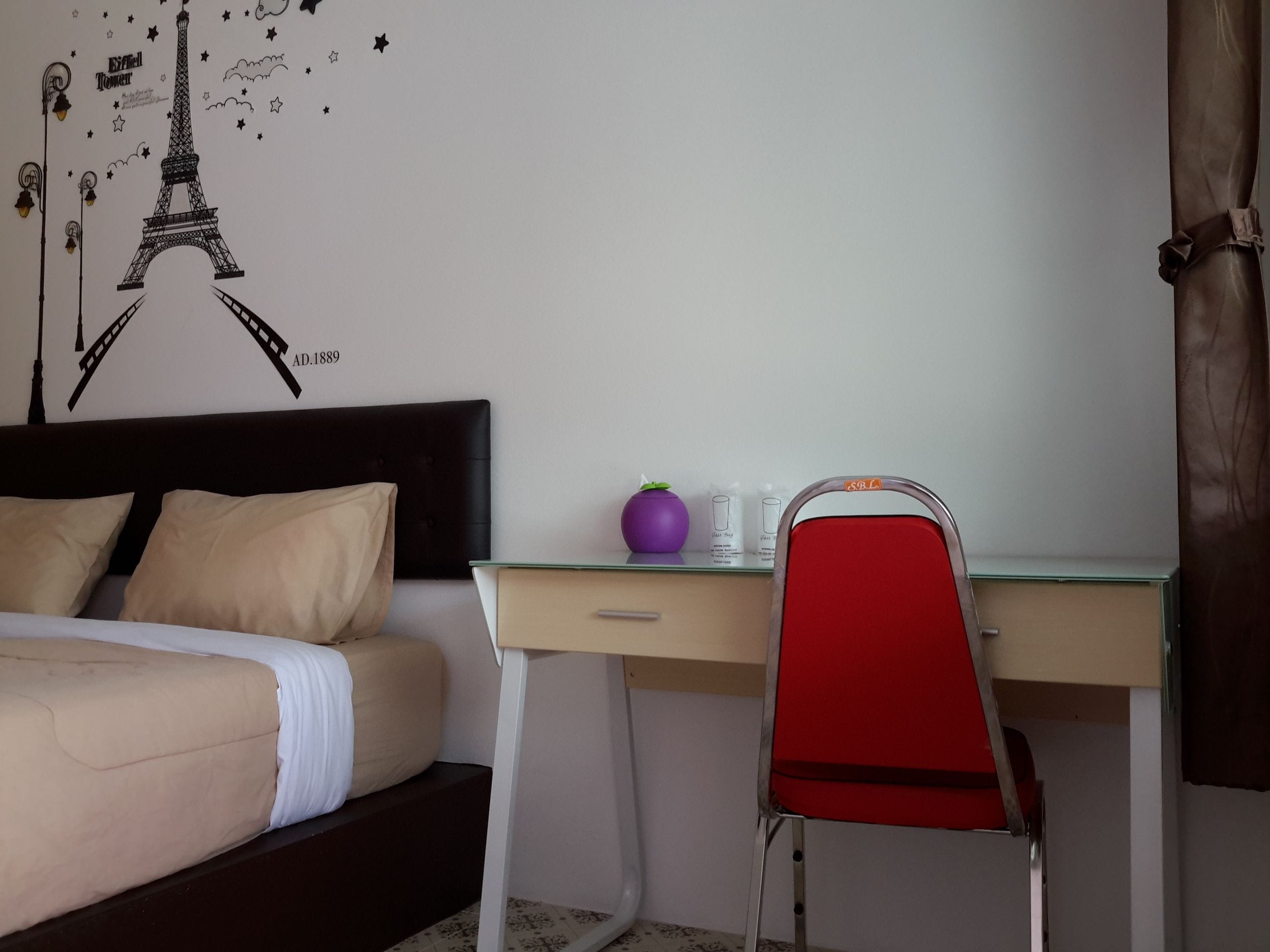 A hotel room with a bed, a desk, a chair, and a wall decoration of the Eiffel Tower.