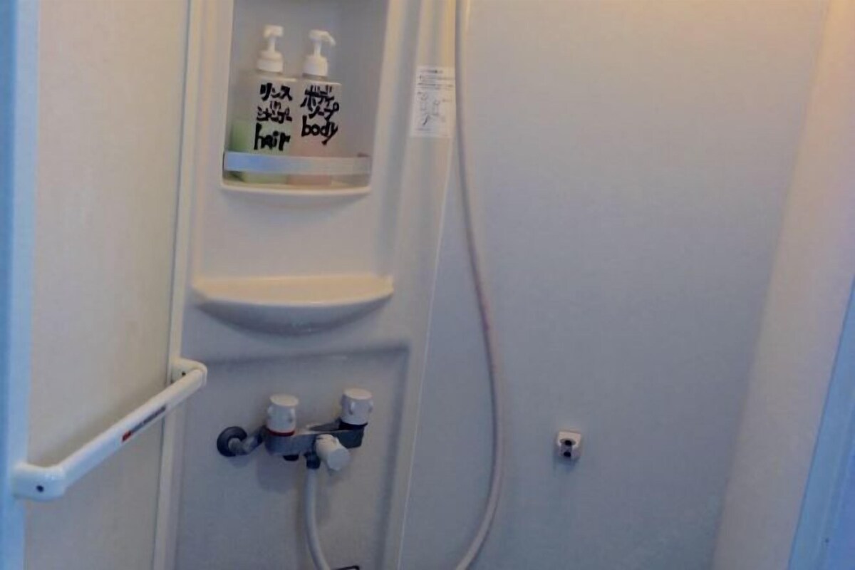 A bathroom with a shower, a soap dispenser, and a towel rack.