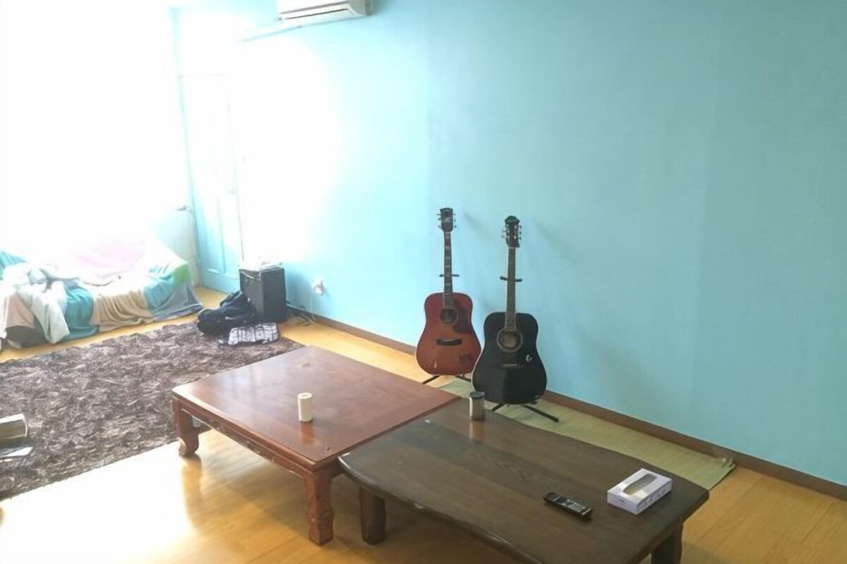 A room with a wooden table, a bench, two guitars, and a small white object on the table.