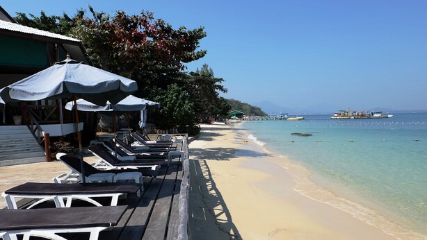 Una terrazza sul mare con sedie a sdraio e ombrelloni, una spiaggia sabbiosa e barche in acqua.
