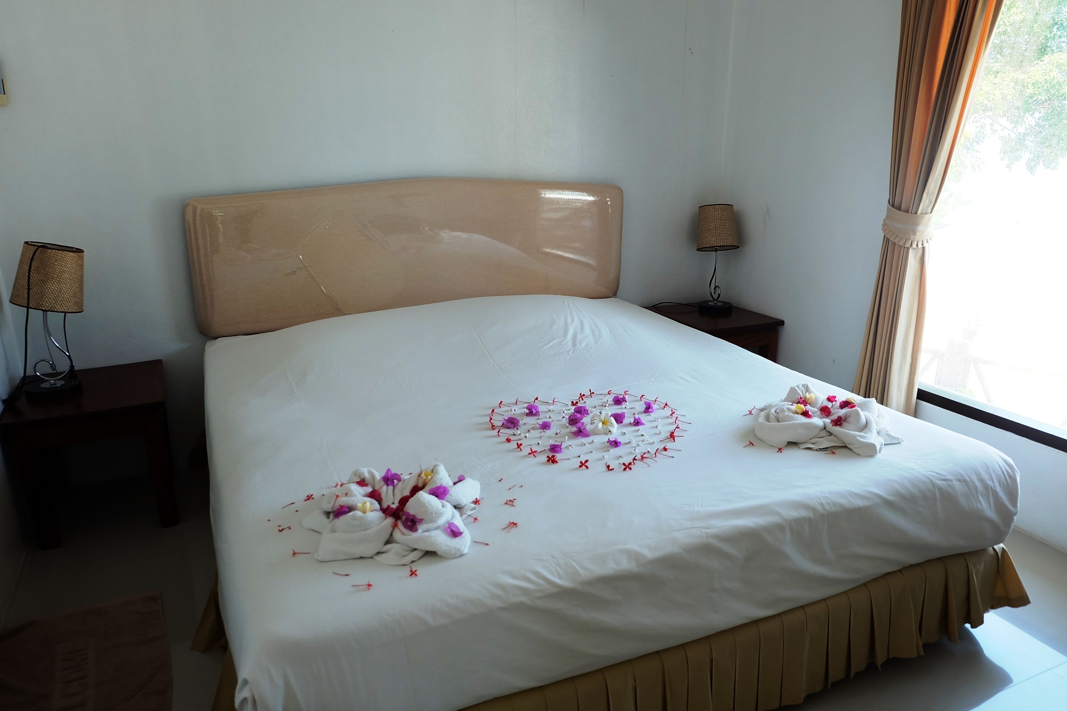 Hotellihuone, jossa on suuri sänky, kaksi yöpöytää valaisimineen ja ikkuna, jossa on verhot.