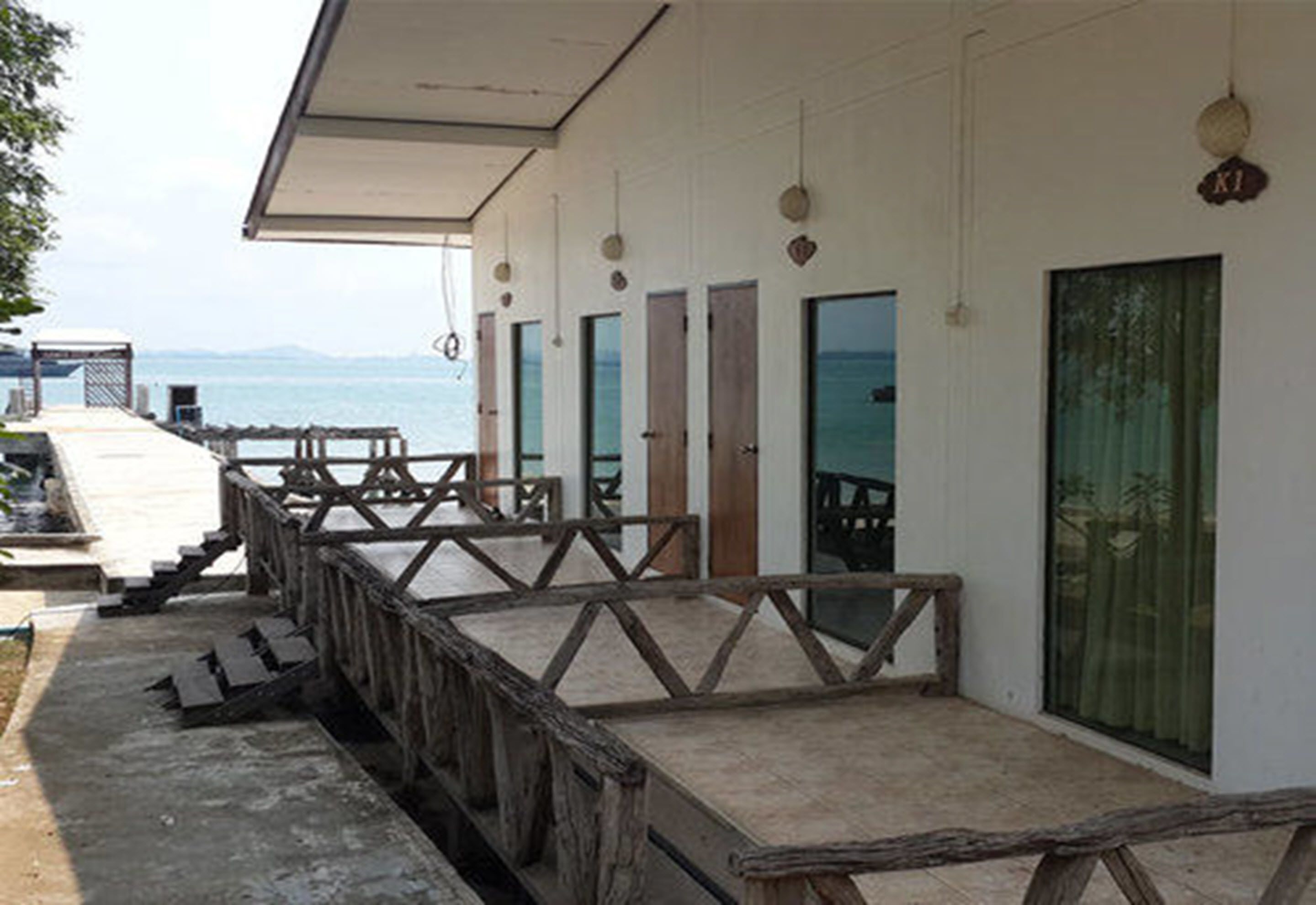 A seaside hotel with a wooden deck, multiple rooms with glass doors, and a view of the sea.