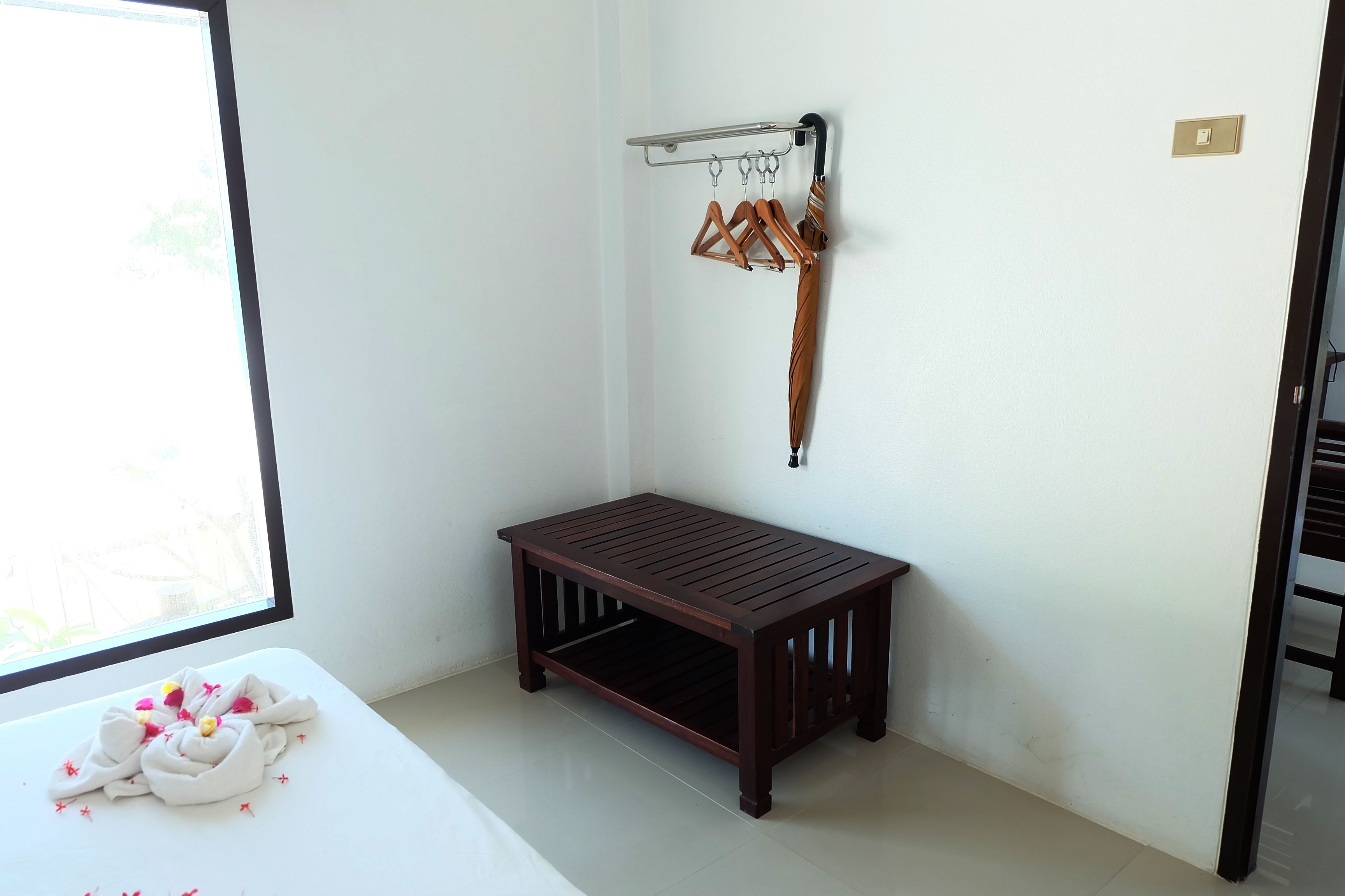 A room with a bed, a wooden bench, a coat rack with hangers, and a window.