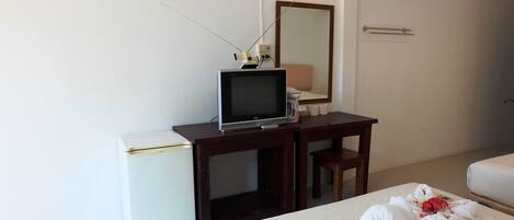 A hotel room with a desk, a television, a small refrigerator, a bed with towels, a mirror, and a bedside table.