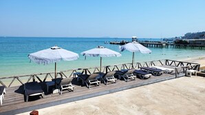 Una terrazza in legno con poltrone e ombrelloni che si affaccia su un mare calmo.